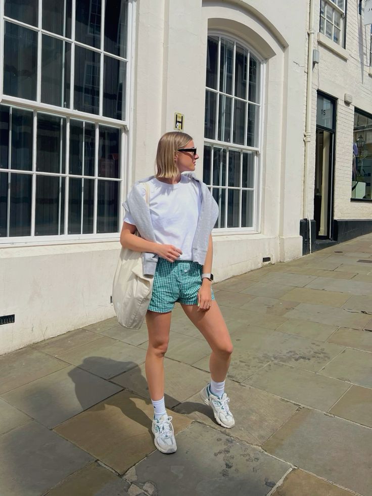 A girl wearing a white t-shirt with green striped shorts, a jacket and a tote bag over her shoulder